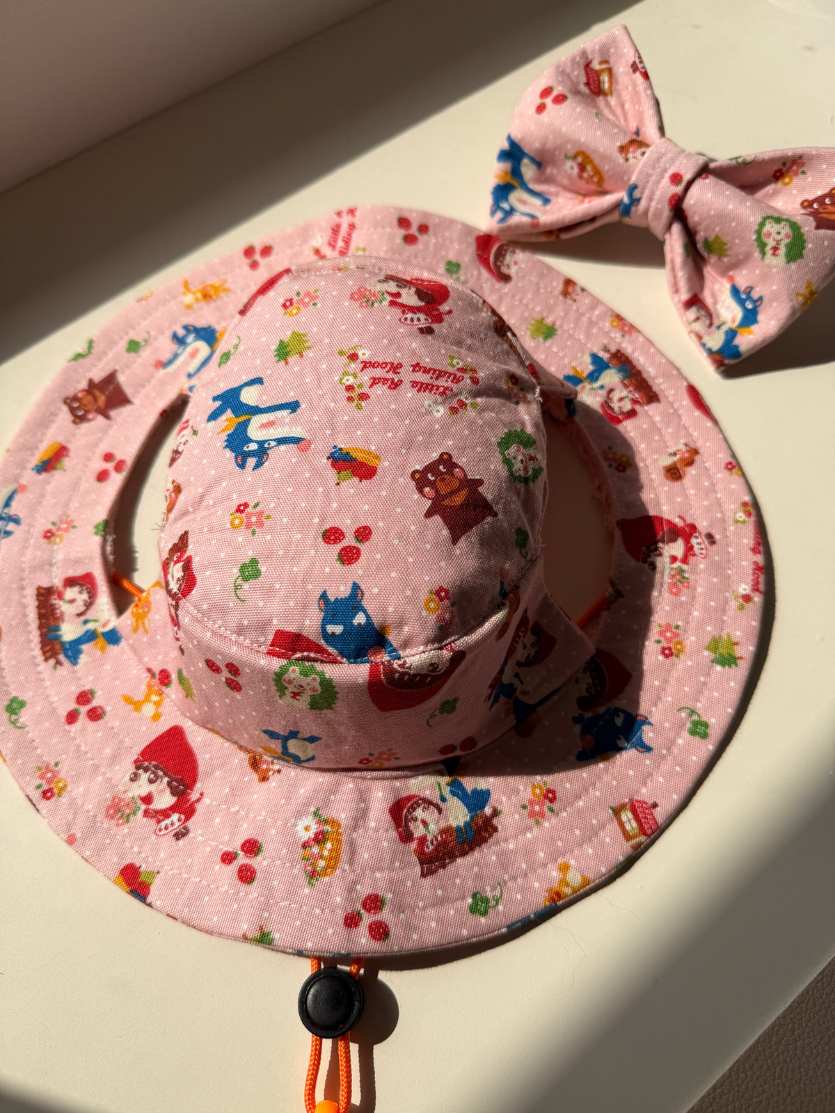 A pink with red riding hood prints bucket hat and bow tie set displayed on a white background.